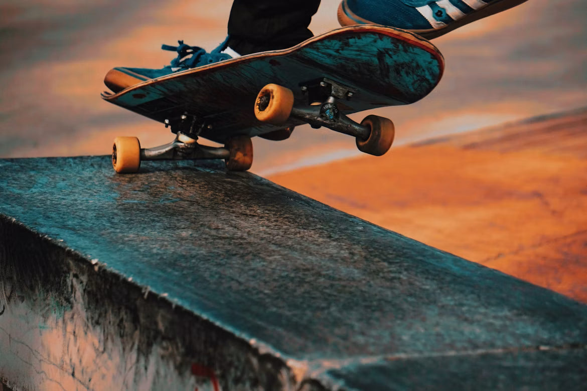 Skateur en grind sur un ledge de skatepark au coucher du soleil, gros plan sur la planche, les trucks et les roues orange